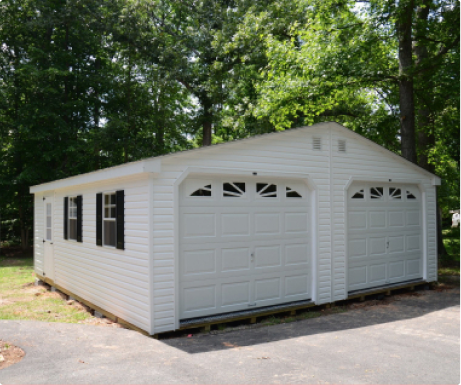 White detached garage with double doors and black shutters in a wooded driveway