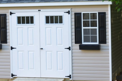 White double barn-style doors beside a window with black shutters on a beige exterior wall
