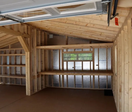 Unfinished wooden garage interior with exposed framing, shelving, and a window.