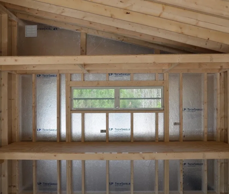Exposed attic framing with sloped wood ceiling and a window opening in an unfinished room