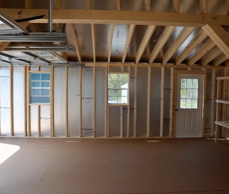 Unfinished interior with exposed wooden framing, insulation, windows, and a white door in a room under construction
