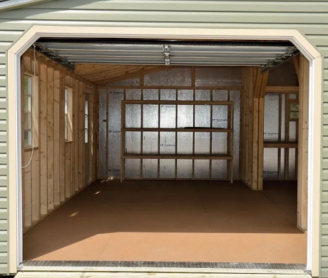 Empty unfinished garage interior with exposed framing, insulation, and brown floor, viewed from the open door