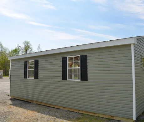 Small gray modular house exterior with black shutters and a blue sky background