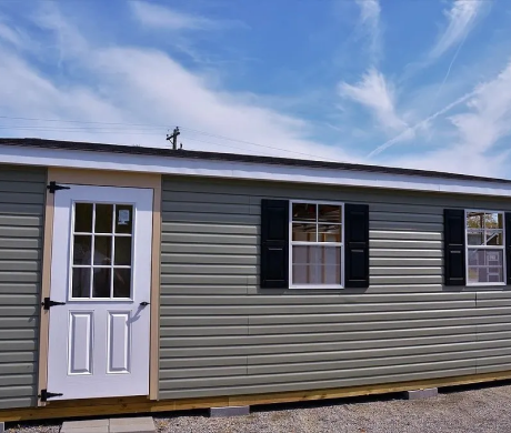 Single-wide gray mobile home with white door and black shutters under a blue sky