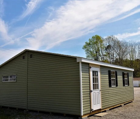 Green single-story mobile home with white trim and a front door, shown outdoors under a blue sky.