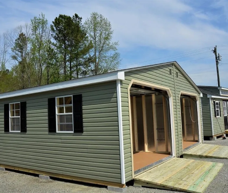 Green prefab shed with open bay door and black shutters on a wooden deck outdoors