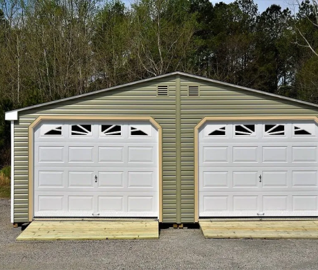 Two-car detached garage with beige siding and white doors on a gravel driveway