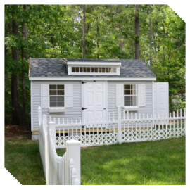 Small white cottage with a picket fence in a green wooded yard