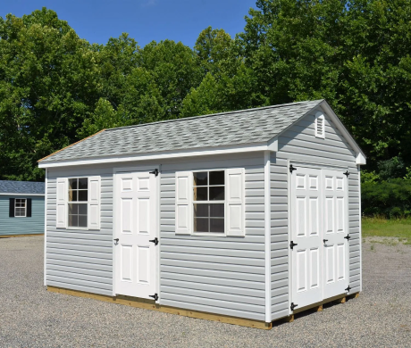 Gray backyard shed with white trim and double doors, set on gravel with trees in the background