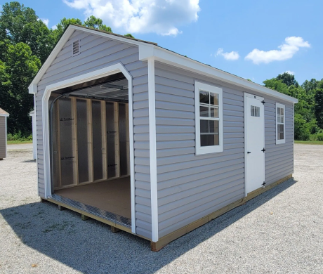 Small gray shed with white trim and open front, standing on gravel under a blue sky