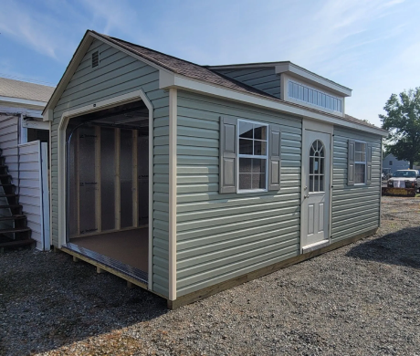 Small gray shed with open garage-style front and white side door on gravel lot