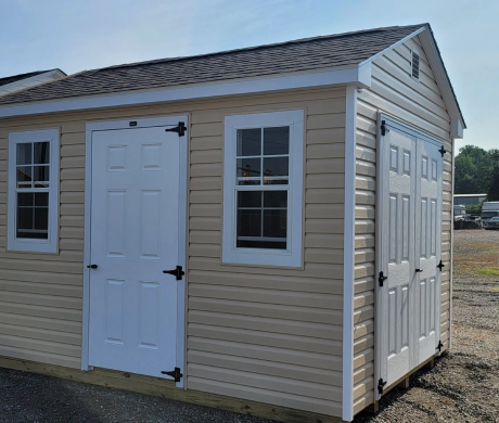 Beige storage shed with white doors and windows on a gravel lot