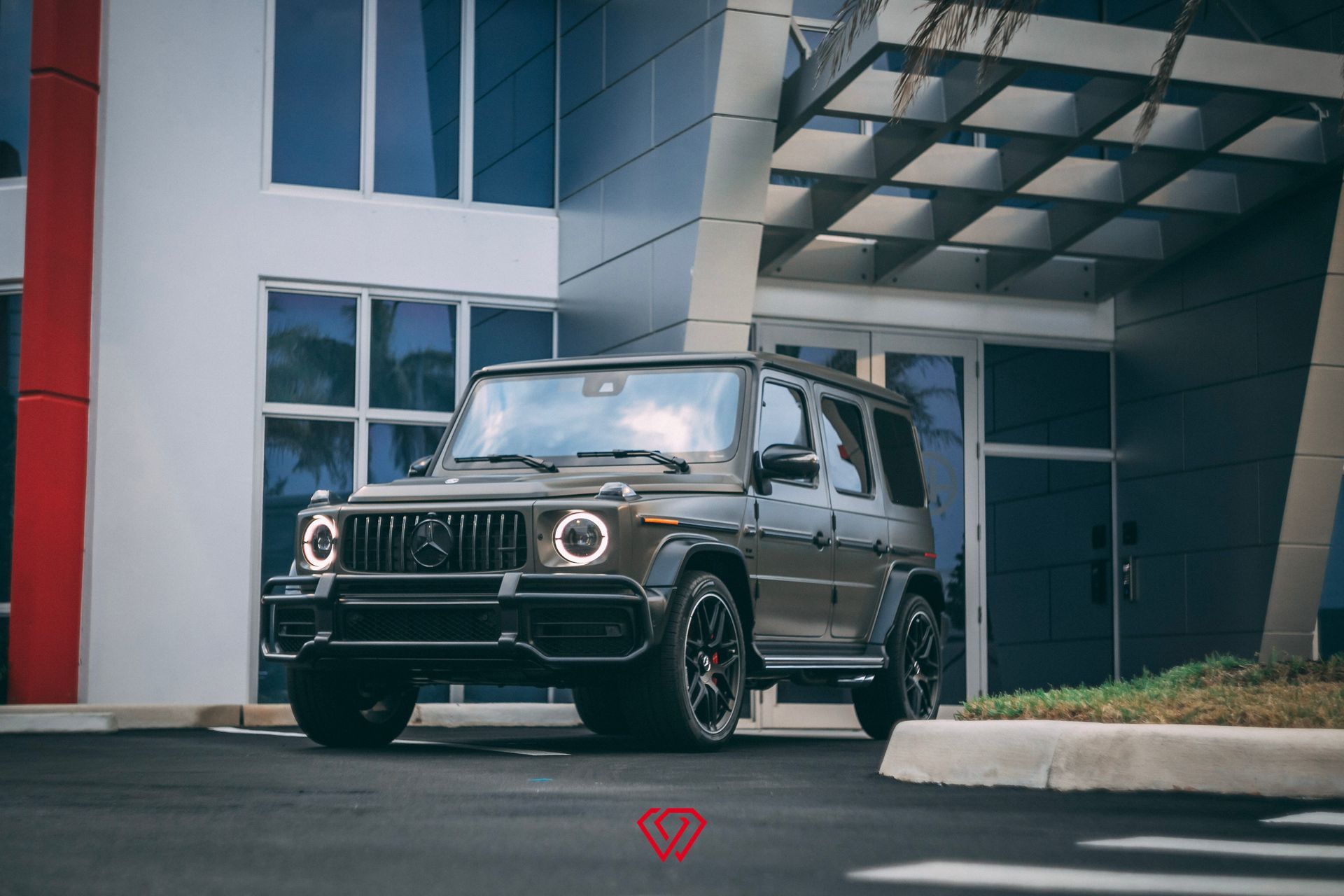 Dark gray Mercedes-Benz G-Wagon parked in front of a modern building with black rims and tinted windows.