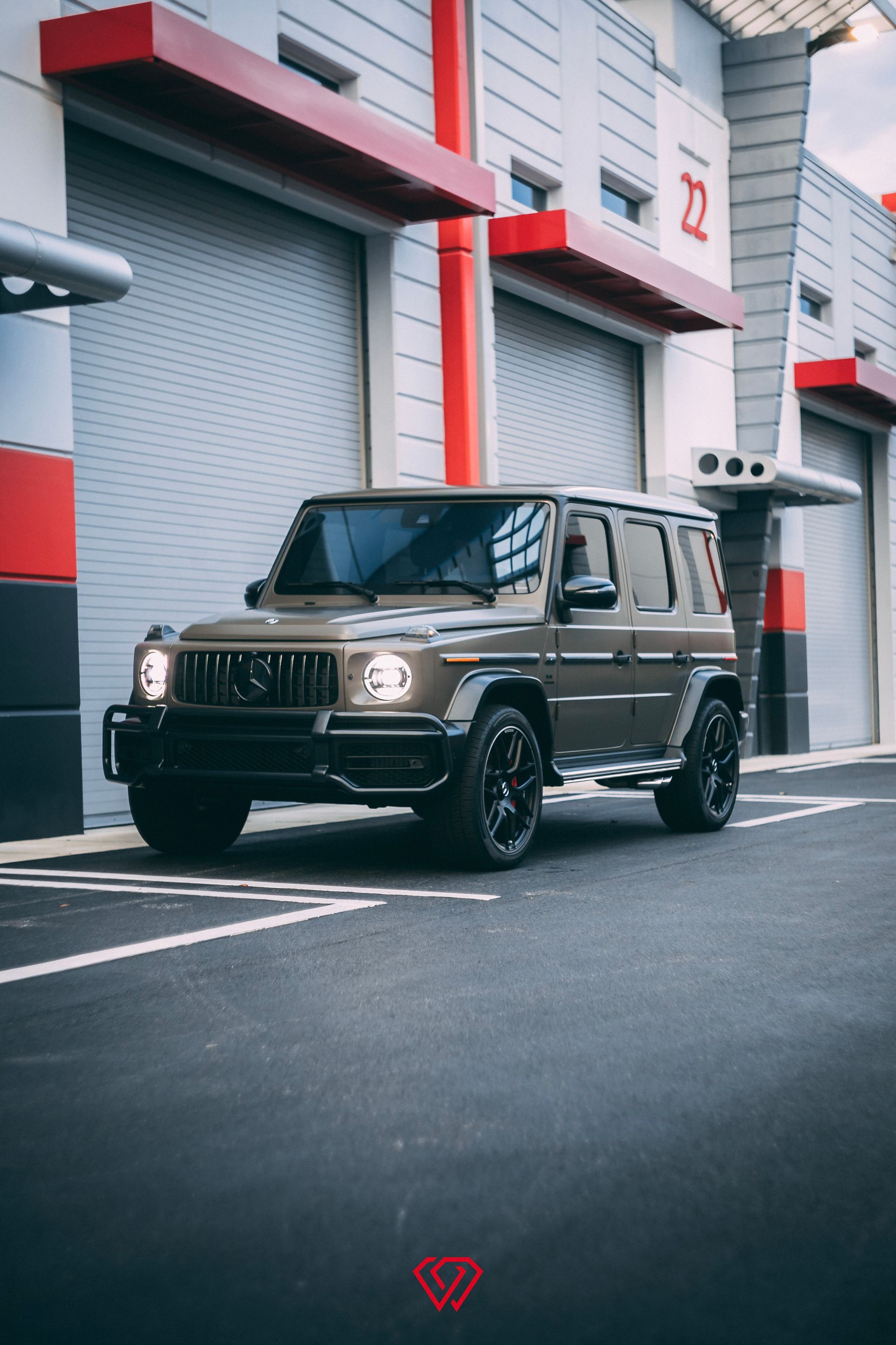 Brown Mercedes-Benz G-Wagon parked in front of a garage with gray doors, and red accents.