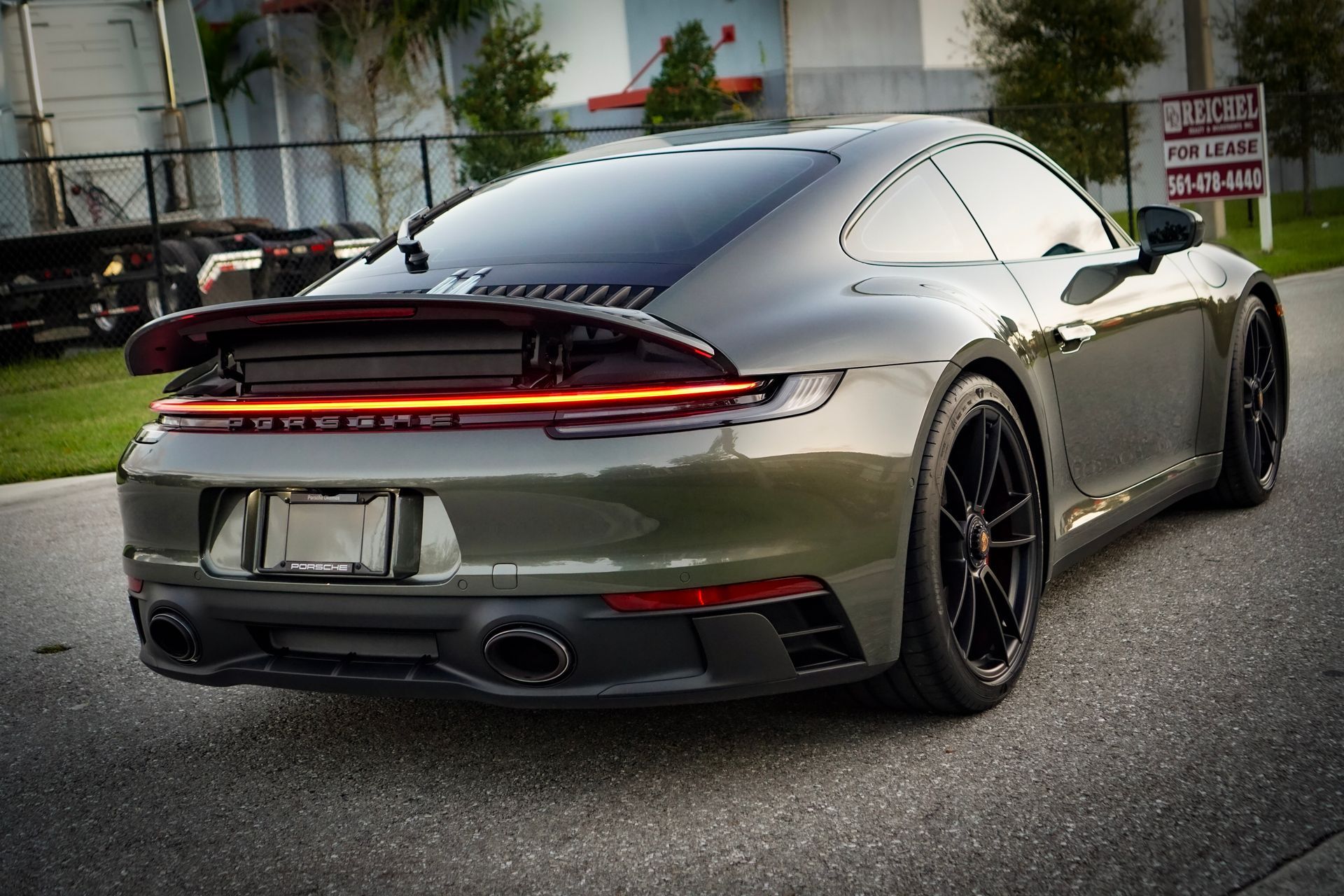 Dark green Porsche 911 coupe on asphalt road, black wheels, rear view.