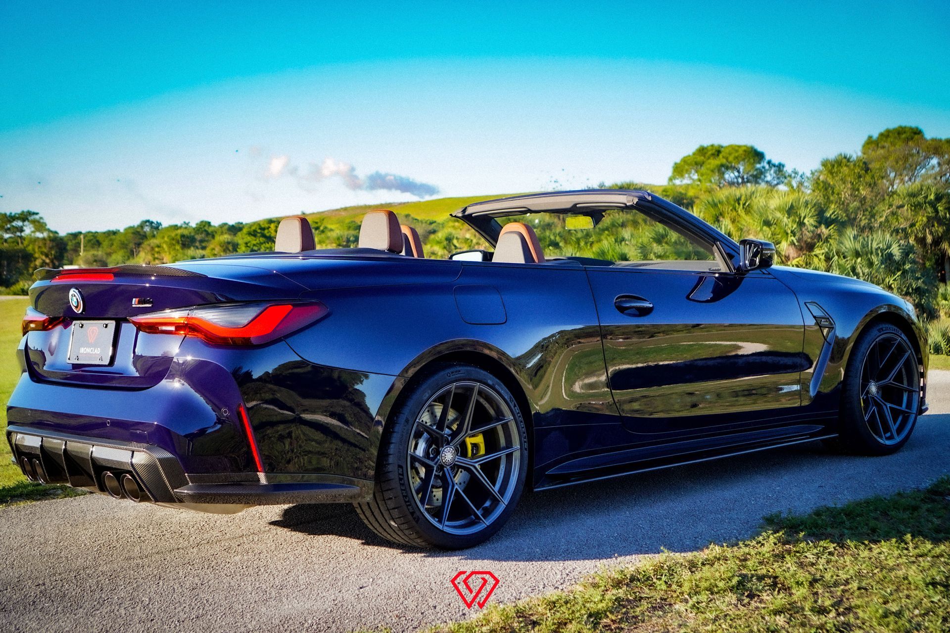 Blue BMW M4 convertible parked on a paved road, top down, with a scenic background.