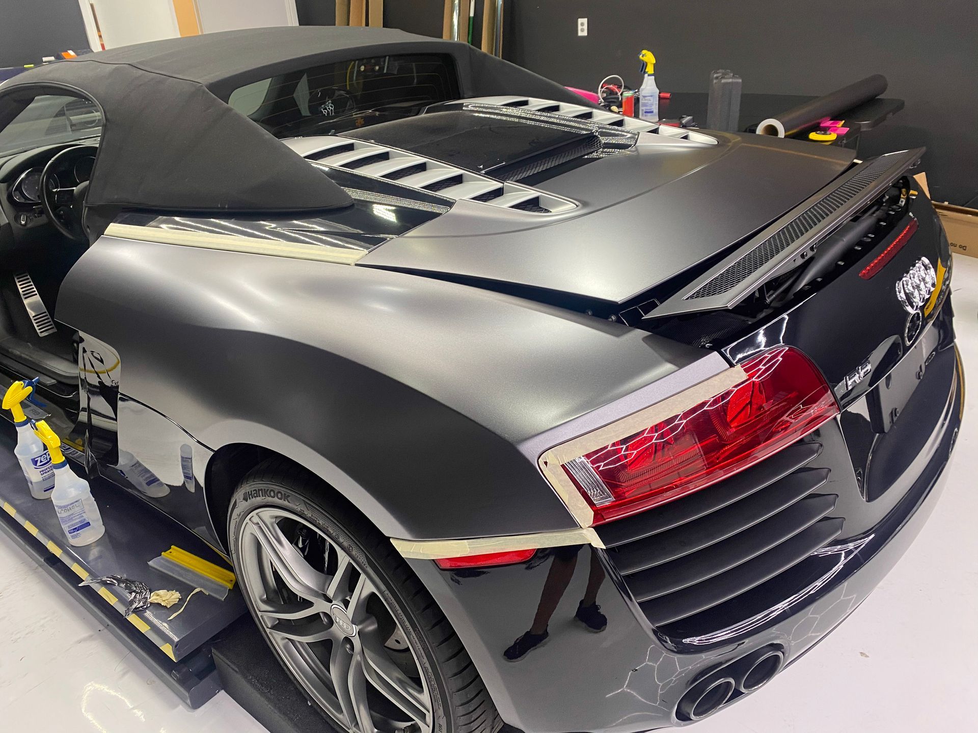Black Audi R8 convertible with the top down, being worked on inside a garage.