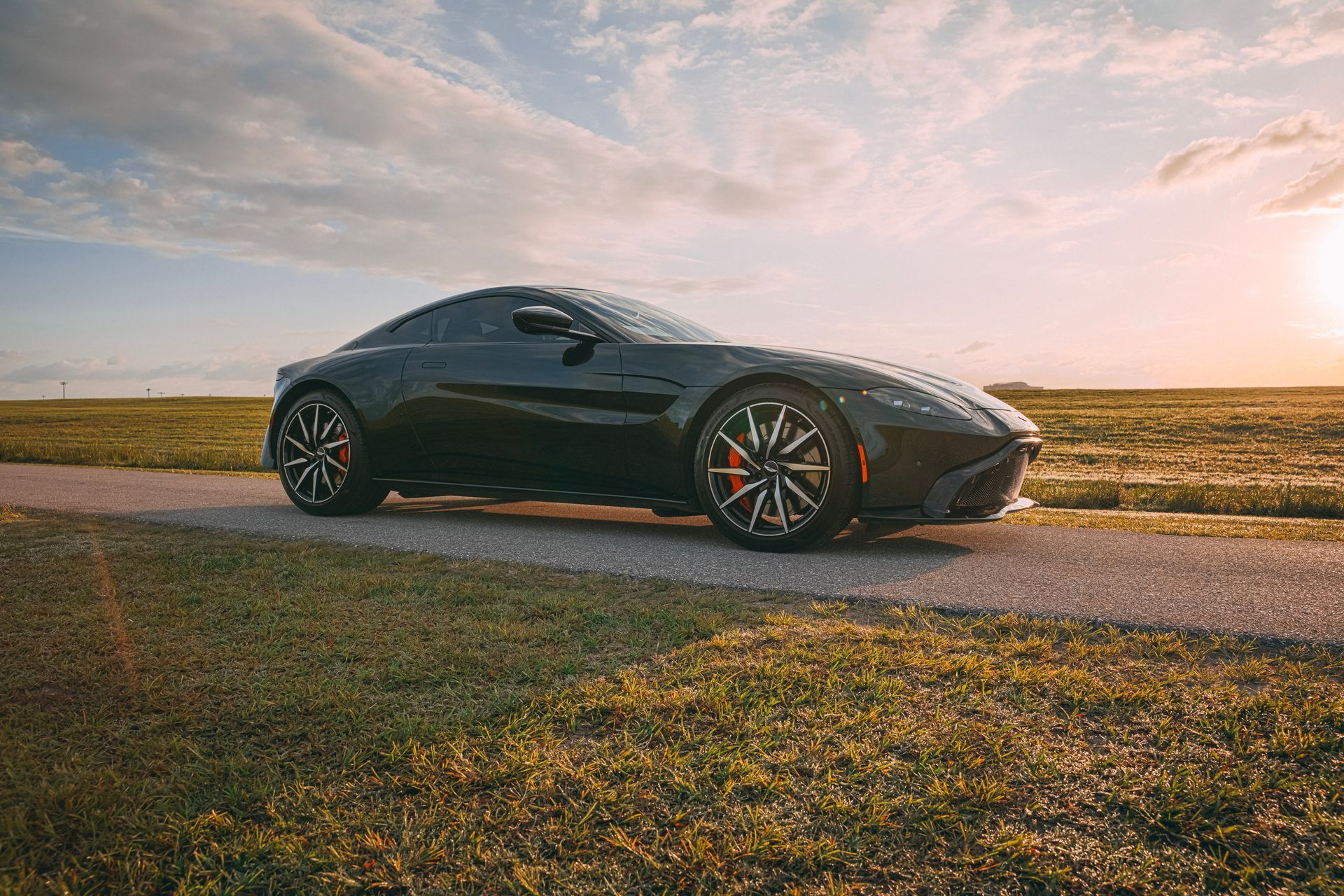 Black Aston Martin sports car on a road, golden sunset in the background.