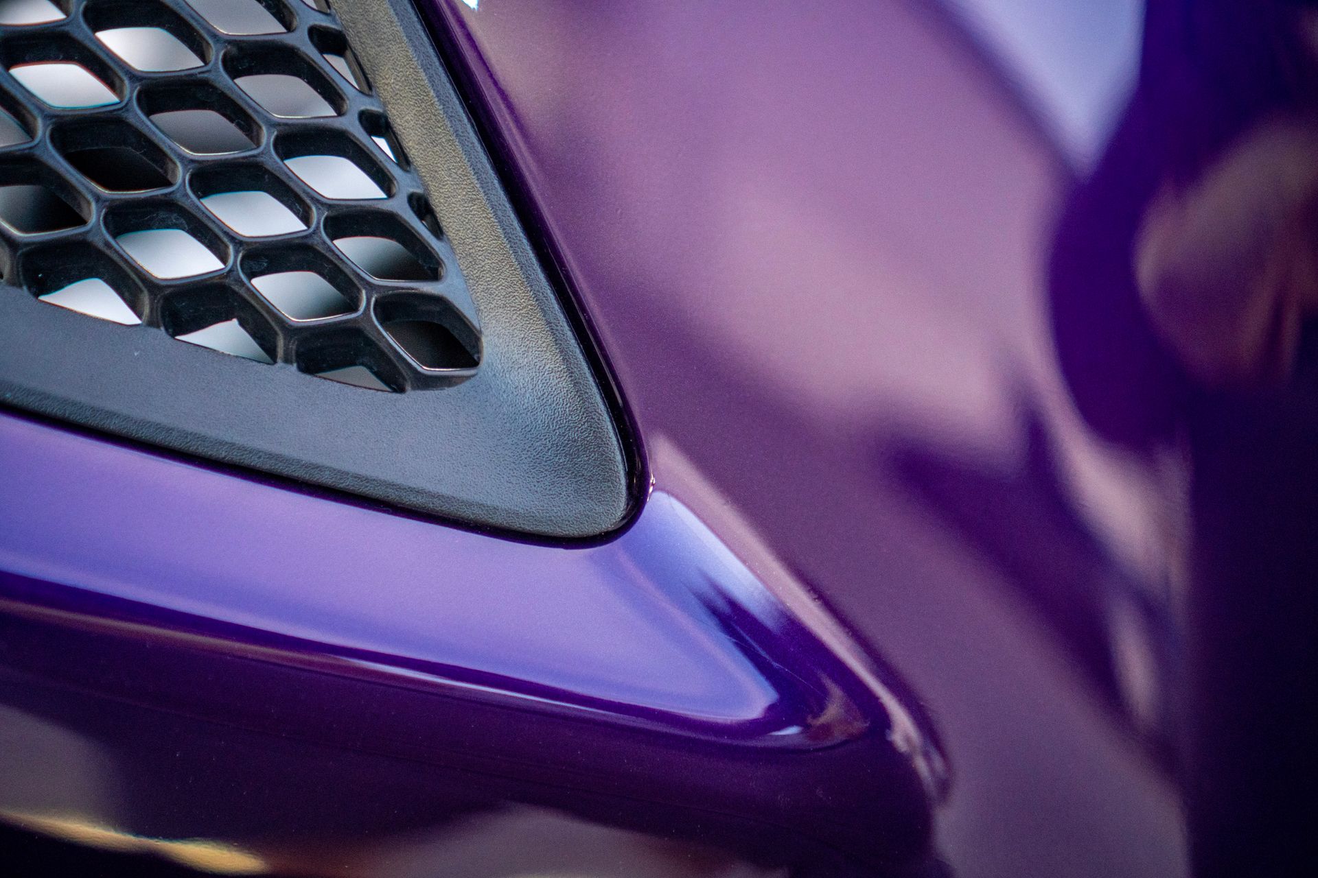 Close-up of a purple car's glossy body and black honeycomb-patterned vent.