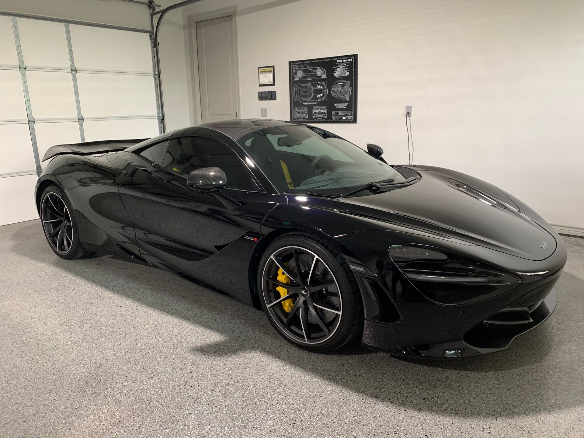 Black McLaren sports car in a garage with yellow brake calipers, gray flooring, and a white garage door.