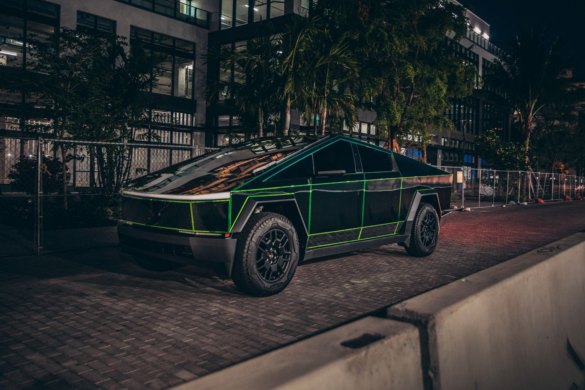 Tesla Cybertruck at night with green neon trim parked on a brick-paved area, near a building.