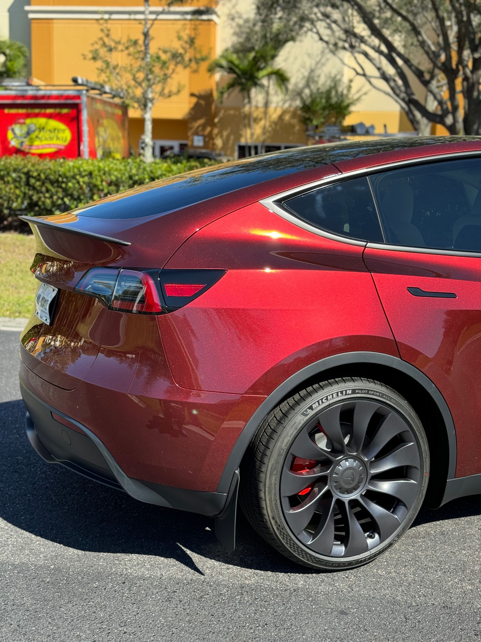 Red Tesla Model Y car with black wheels, parked in front of a building.