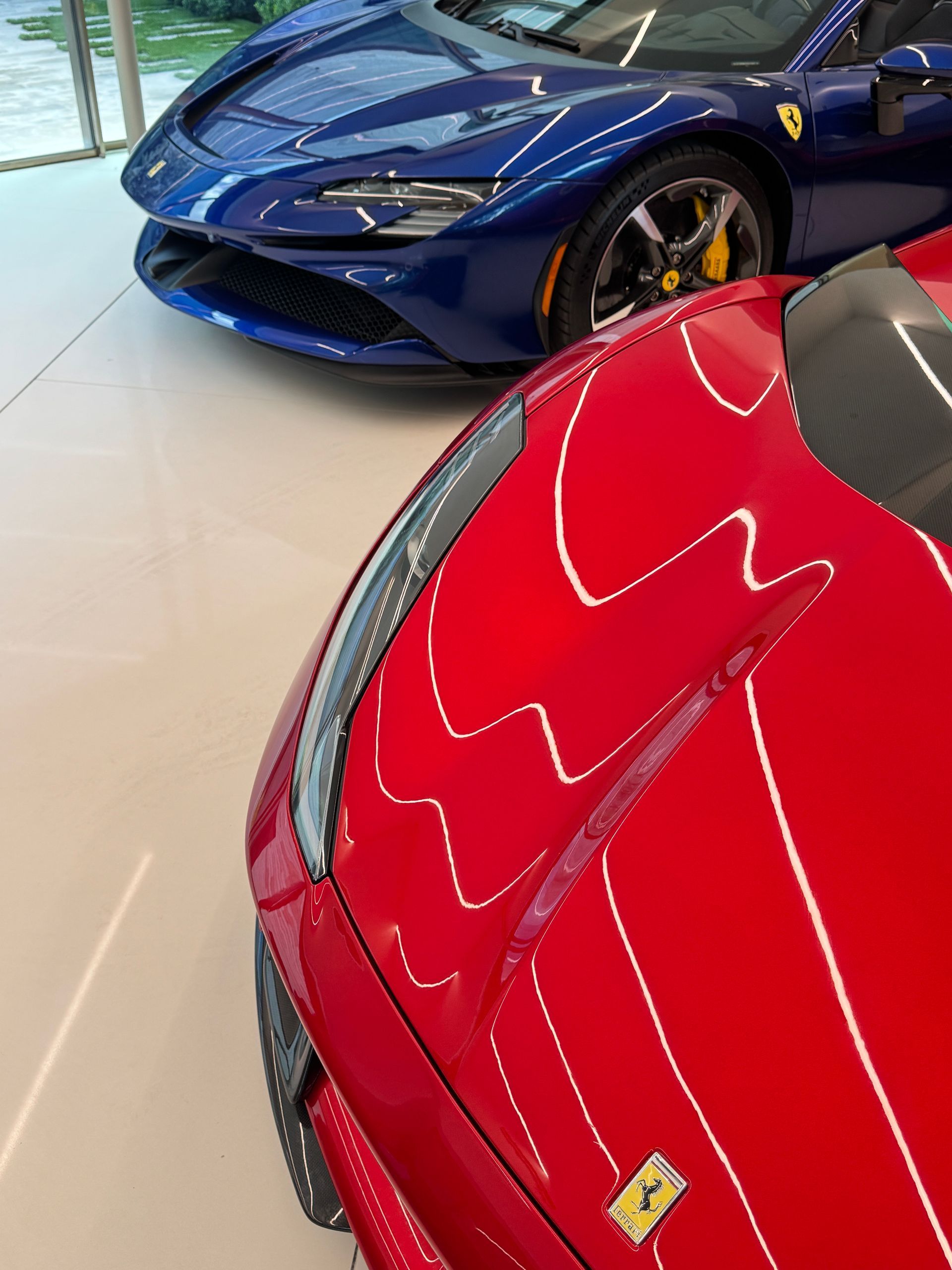 Red Ferrari in the foreground, blue Ferrari in the background, both on display in a showroom.