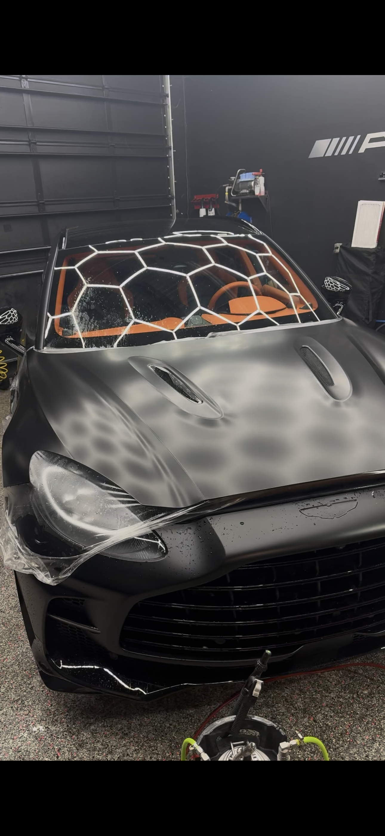 Black car with honeycomb pattern on windshield, in a dark garage.