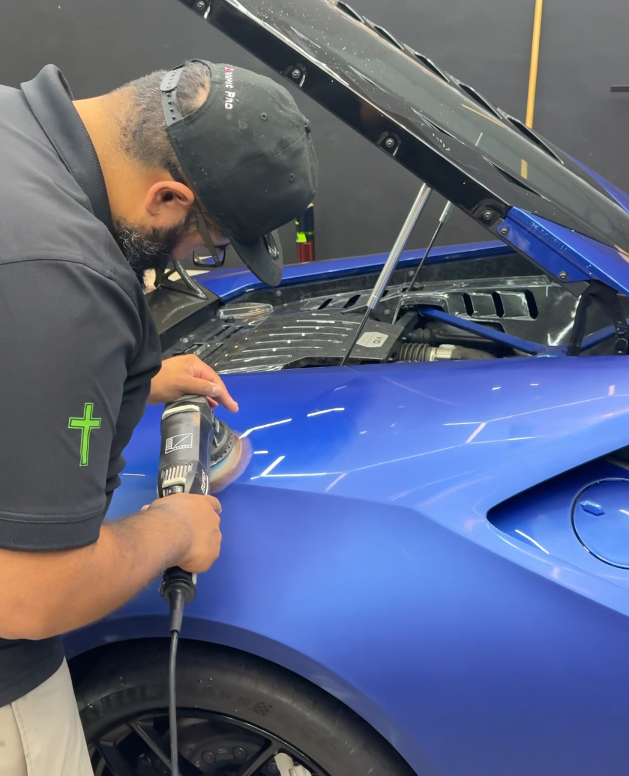 Person polishing a blue sports car with a power tool.