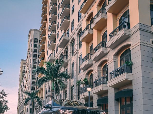 Luxury apartment building with palm trees and a car parked in front.