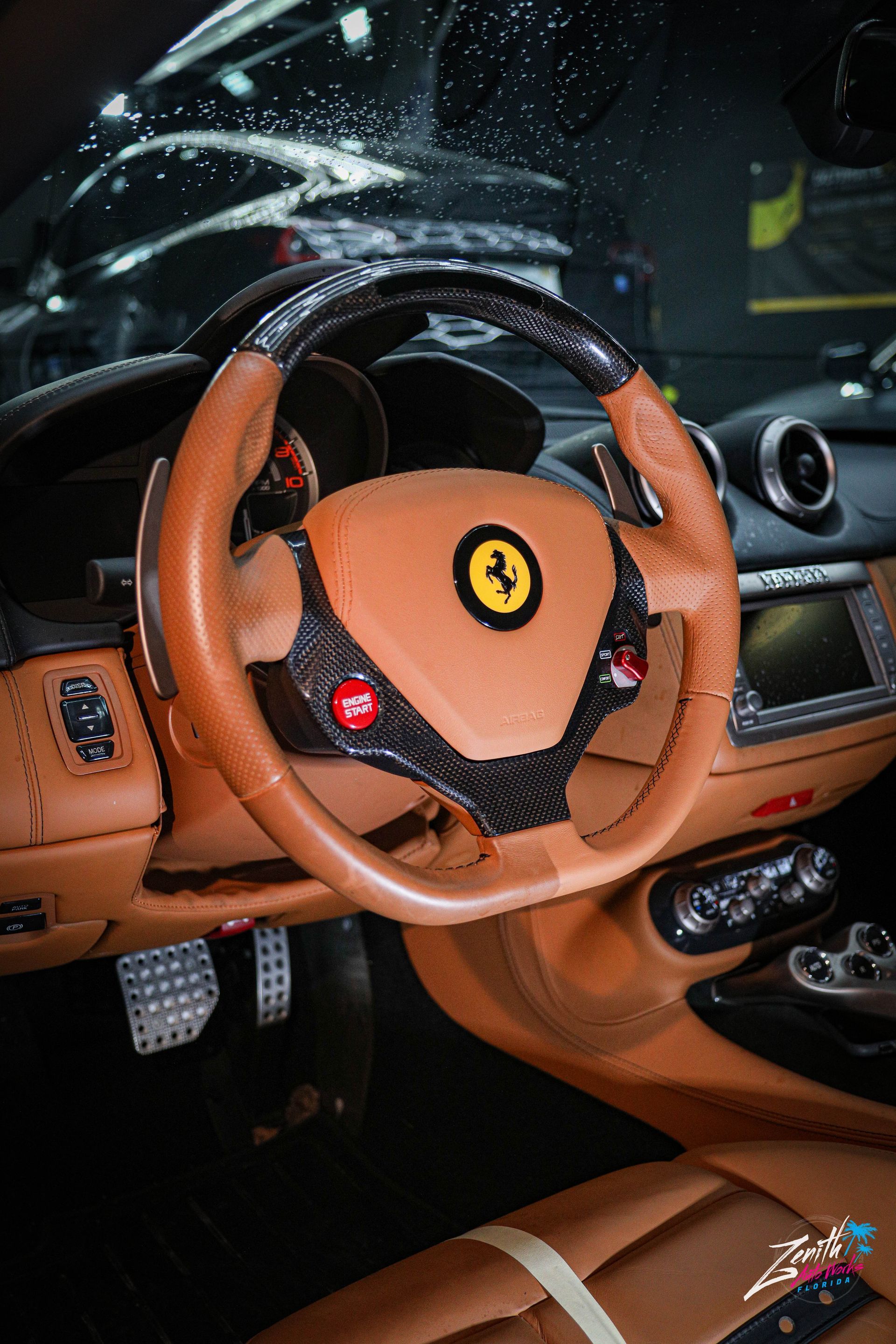 Tan Ferrari interior with steering wheel, red button, and dashboard.