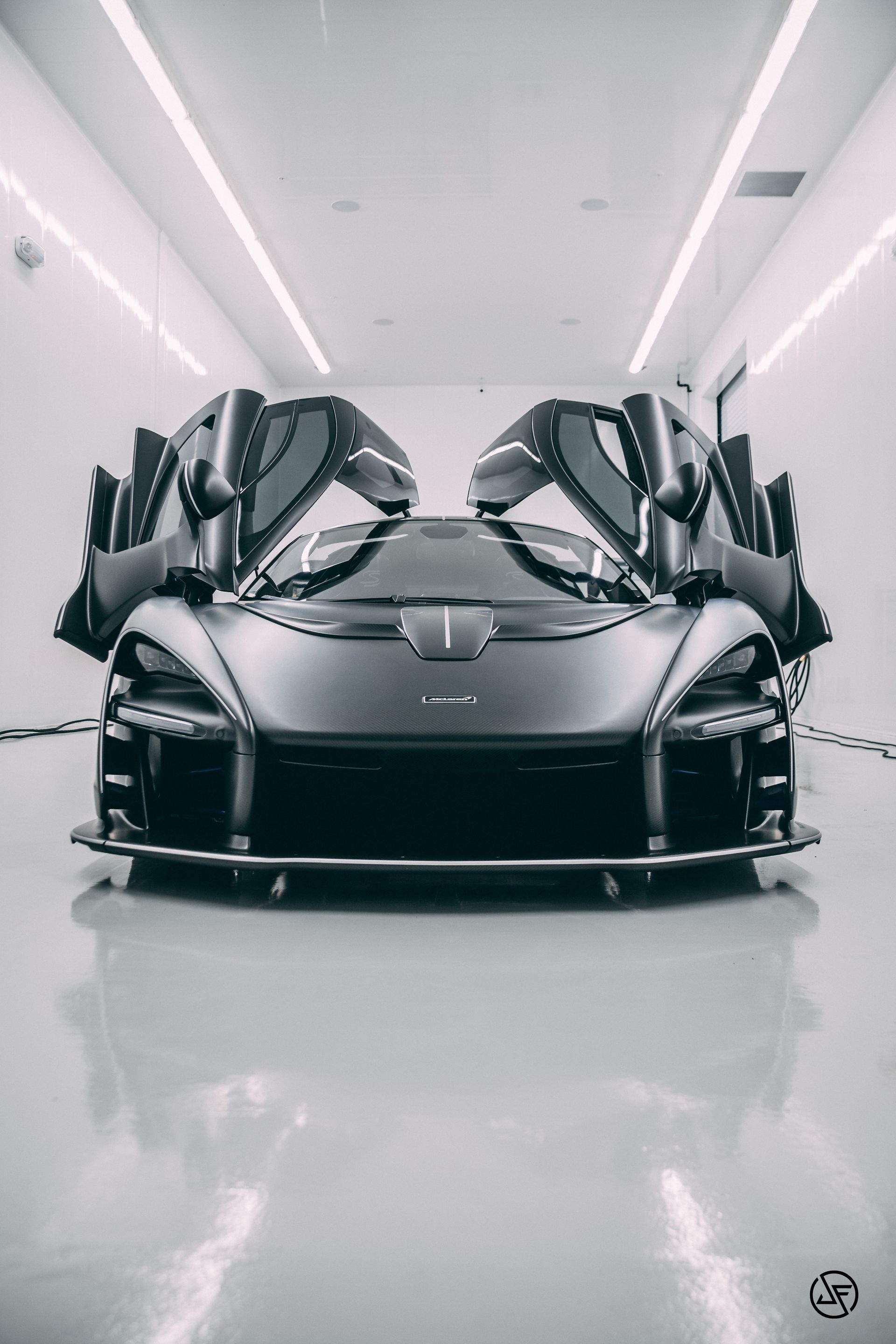Black McLaren Senna with doors open in a white, well-lit showroom.