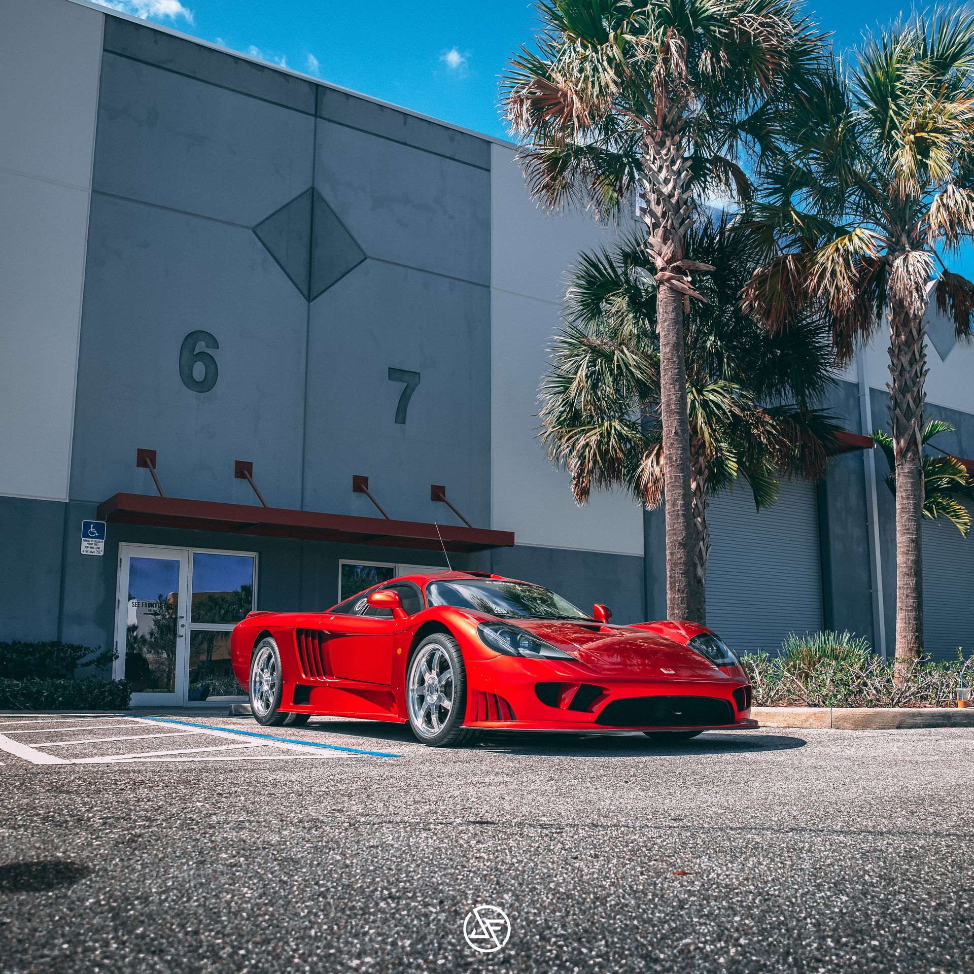 Red Saleen S7 parked in front of a gray industrial building with palm trees.