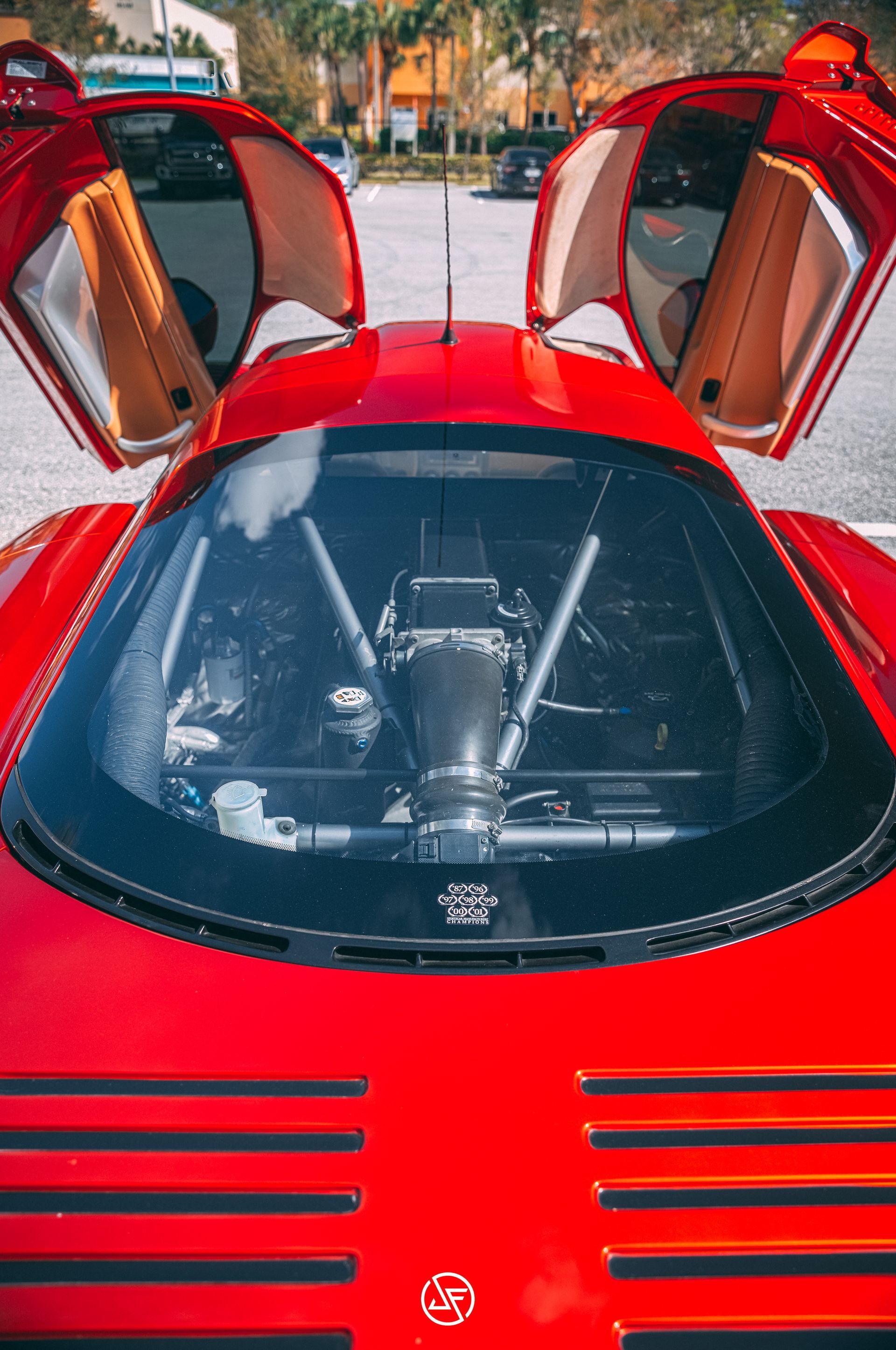 Red sports car with gullwing doors open, revealing the engine.