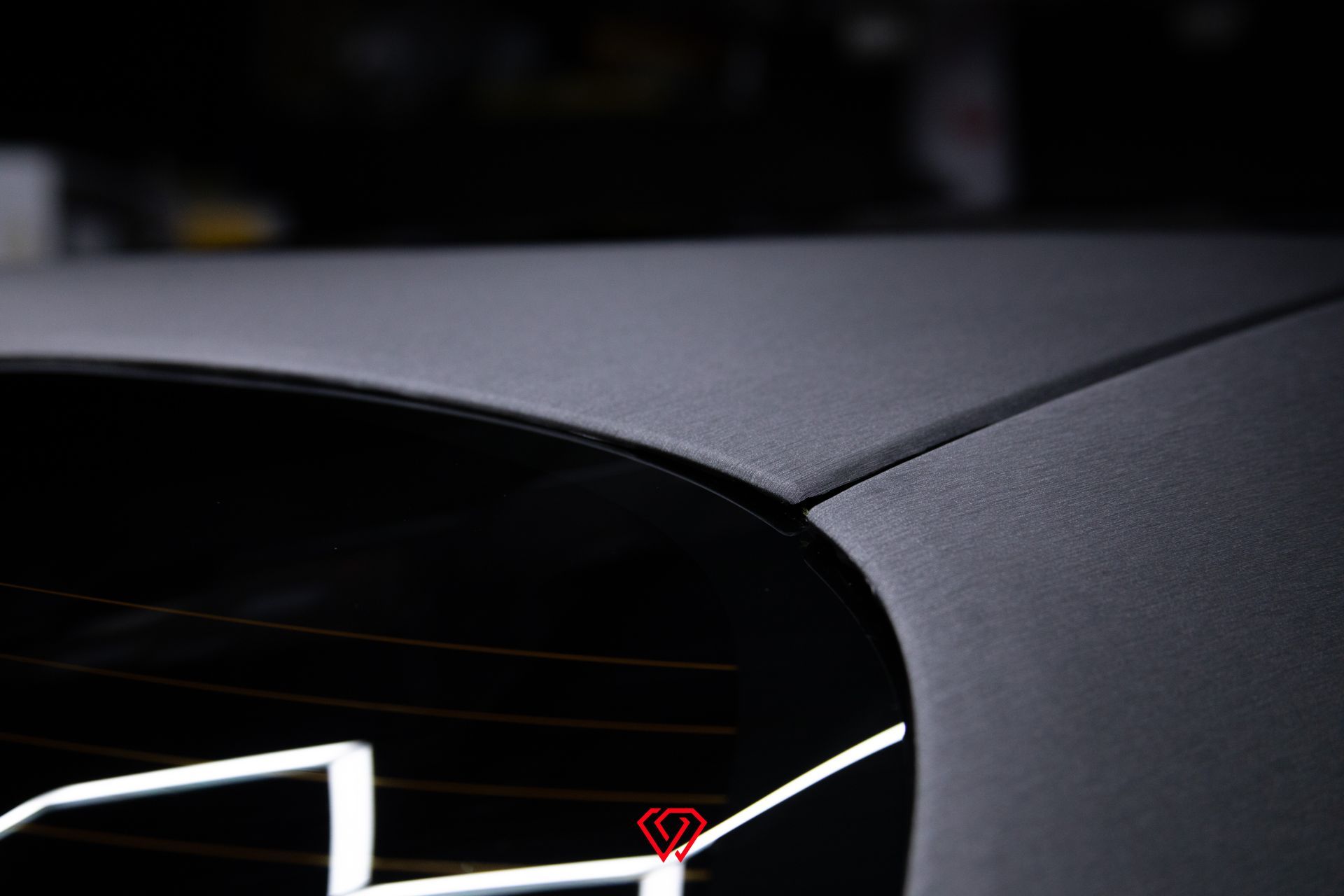 Close-up of a black car roof and rear window. A red location pin is overlaid near the bottom.