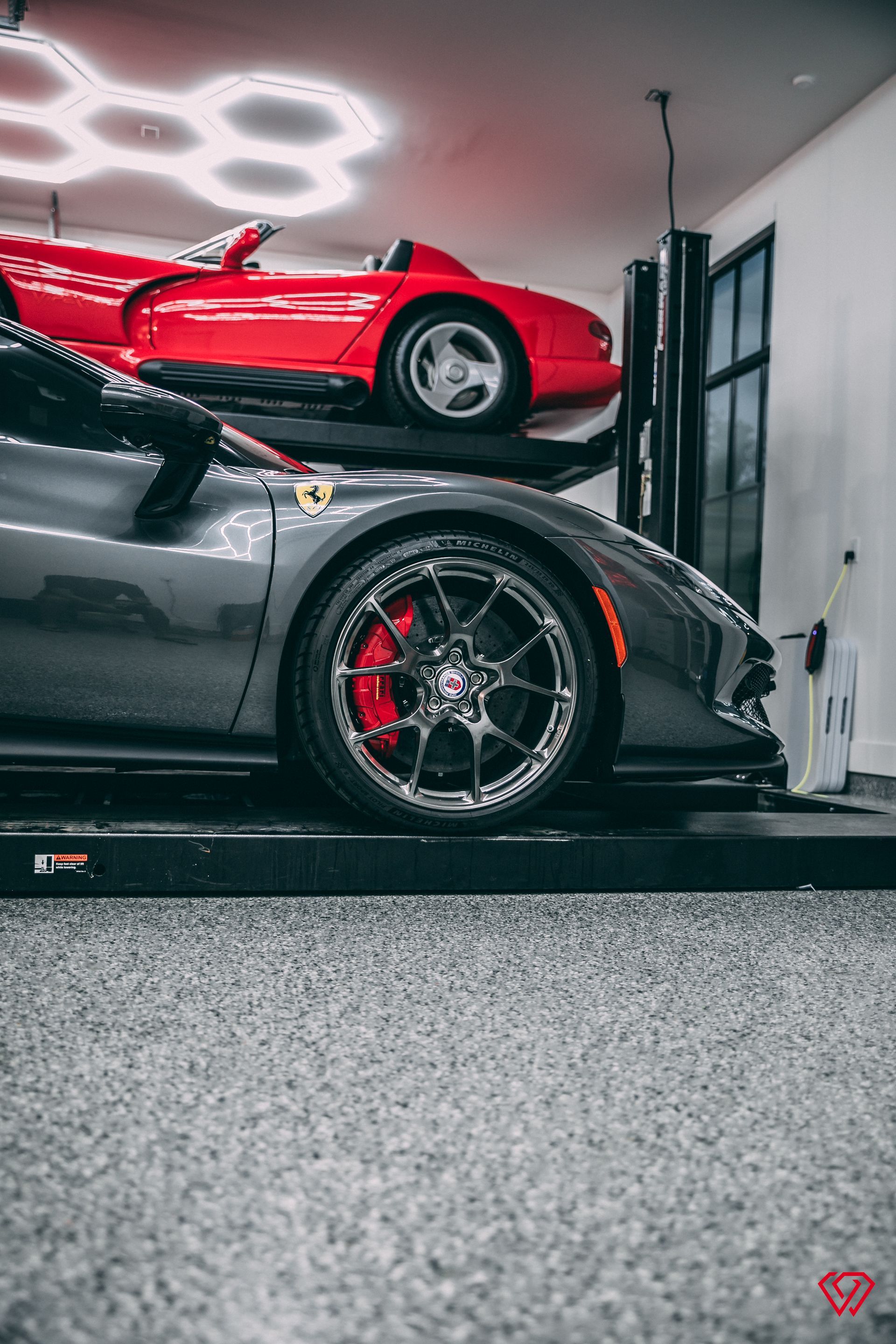 Gray Ferrari below a red convertible on a car lift in a garage.