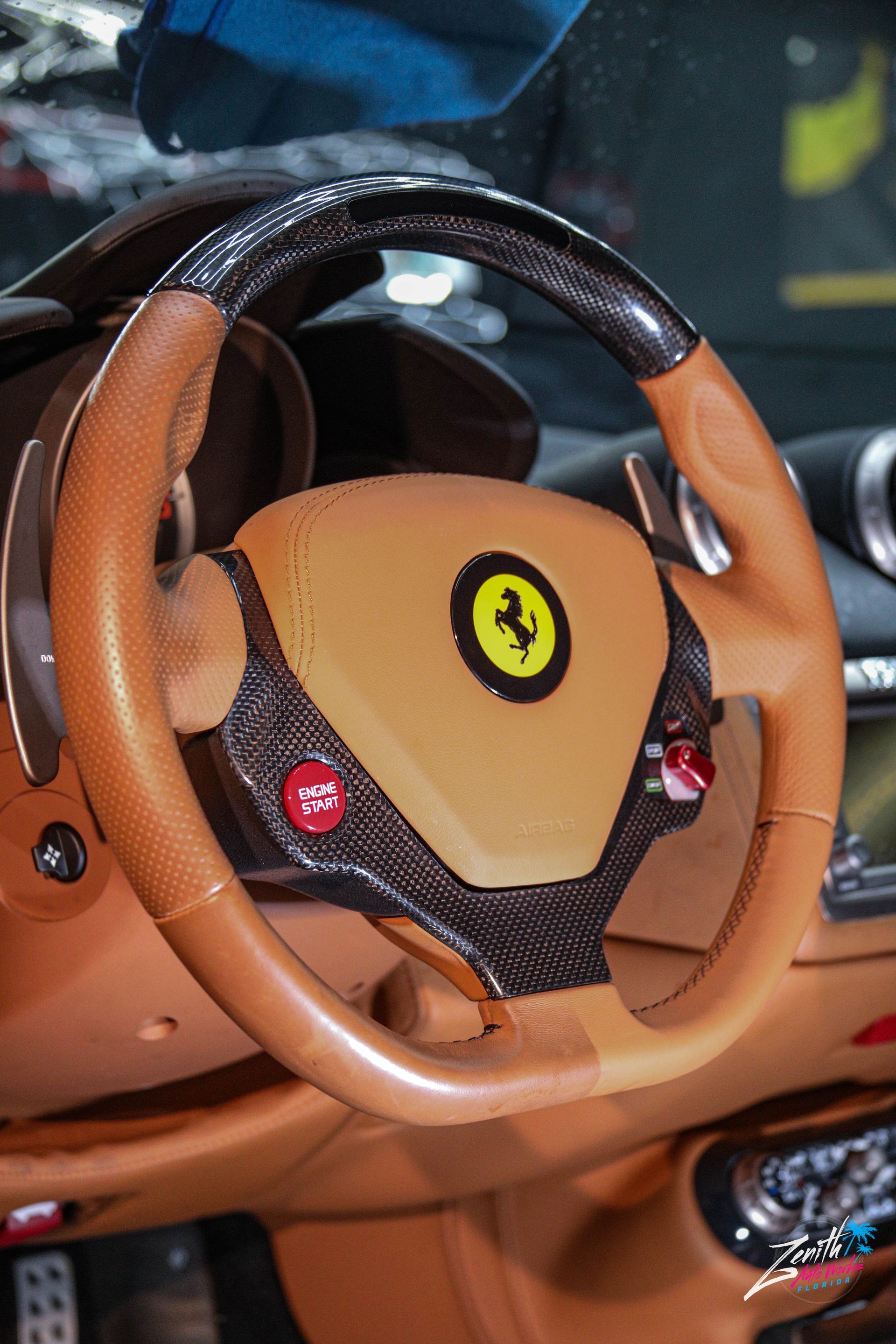 Tan leather Ferrari steering wheel with carbon fiber accents, featuring the iconic prancing horse logo.
