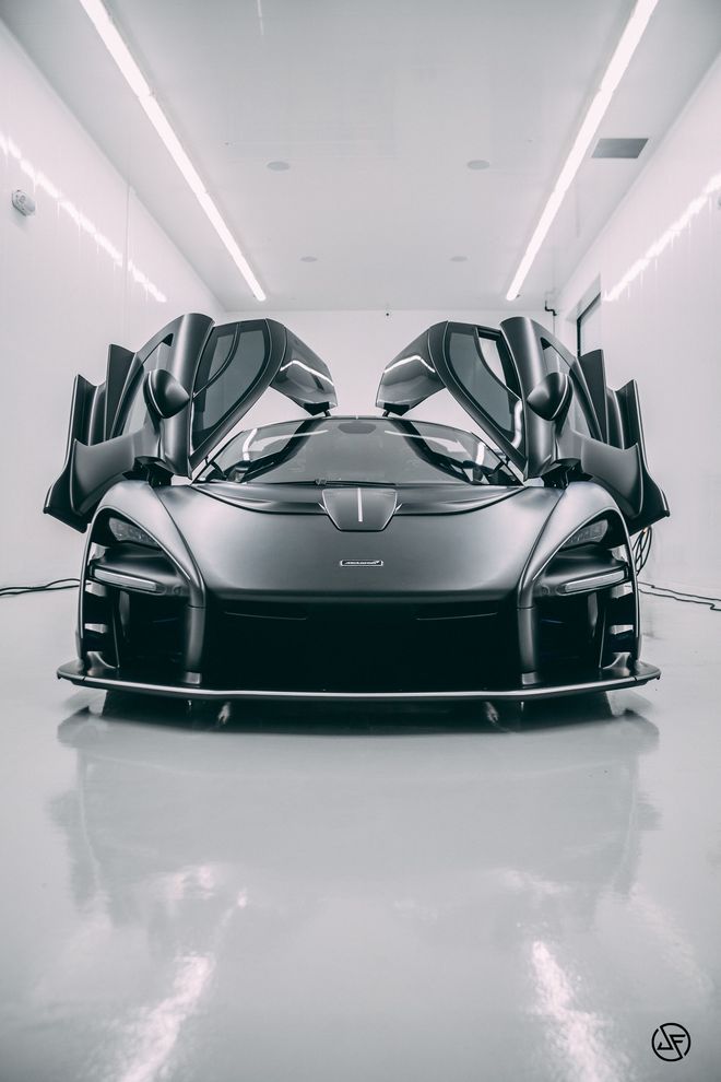 Black McLaren Senna with doors open, in a bright, modern garage.