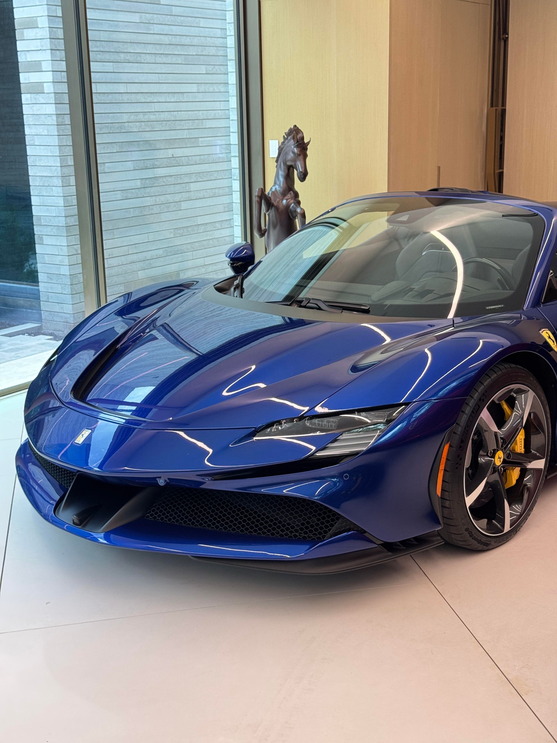 Blue Ferrari sports car parked inside a showroom, with a sculpture of a horse in the background.