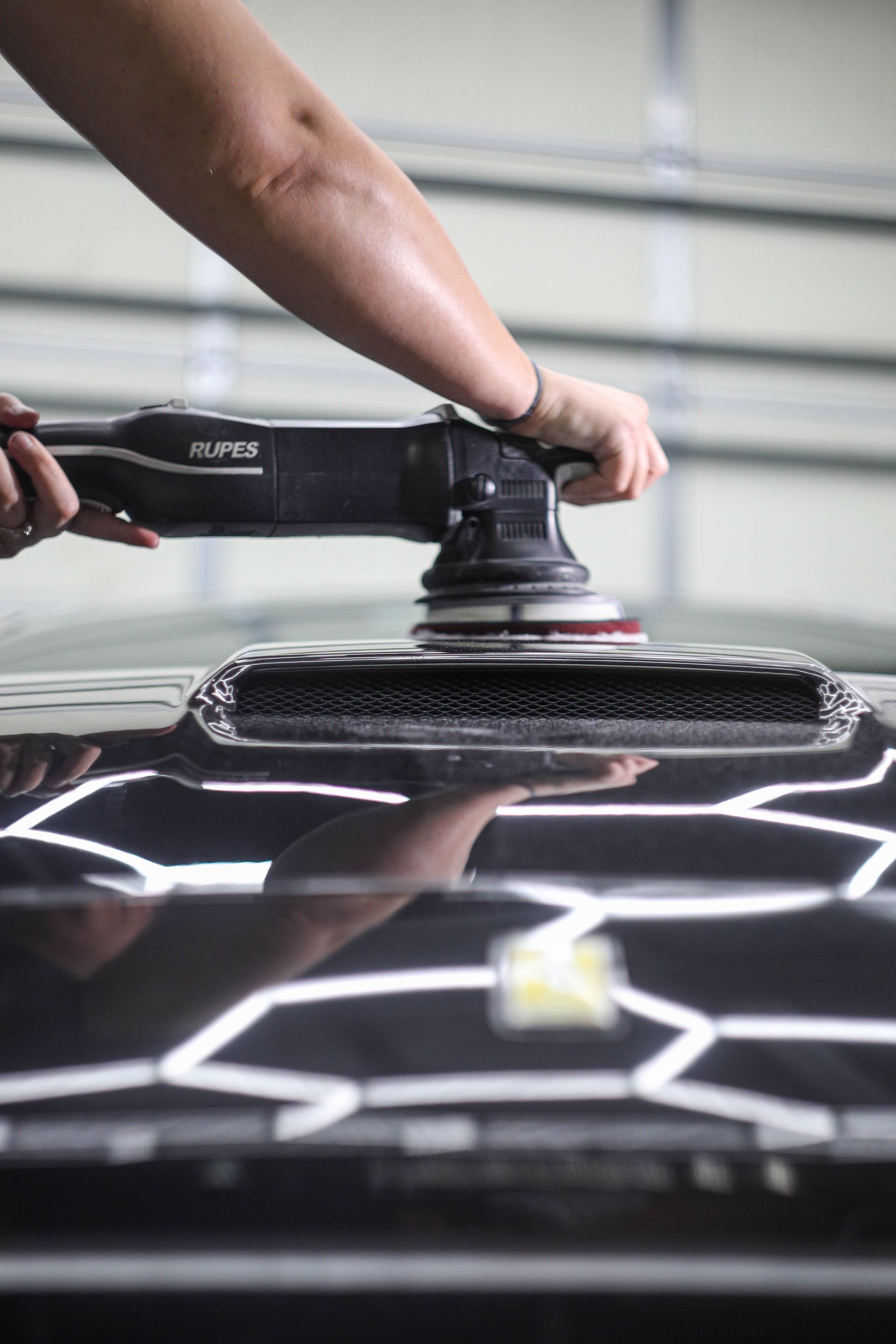 Person polishing a black car hood with a machine.