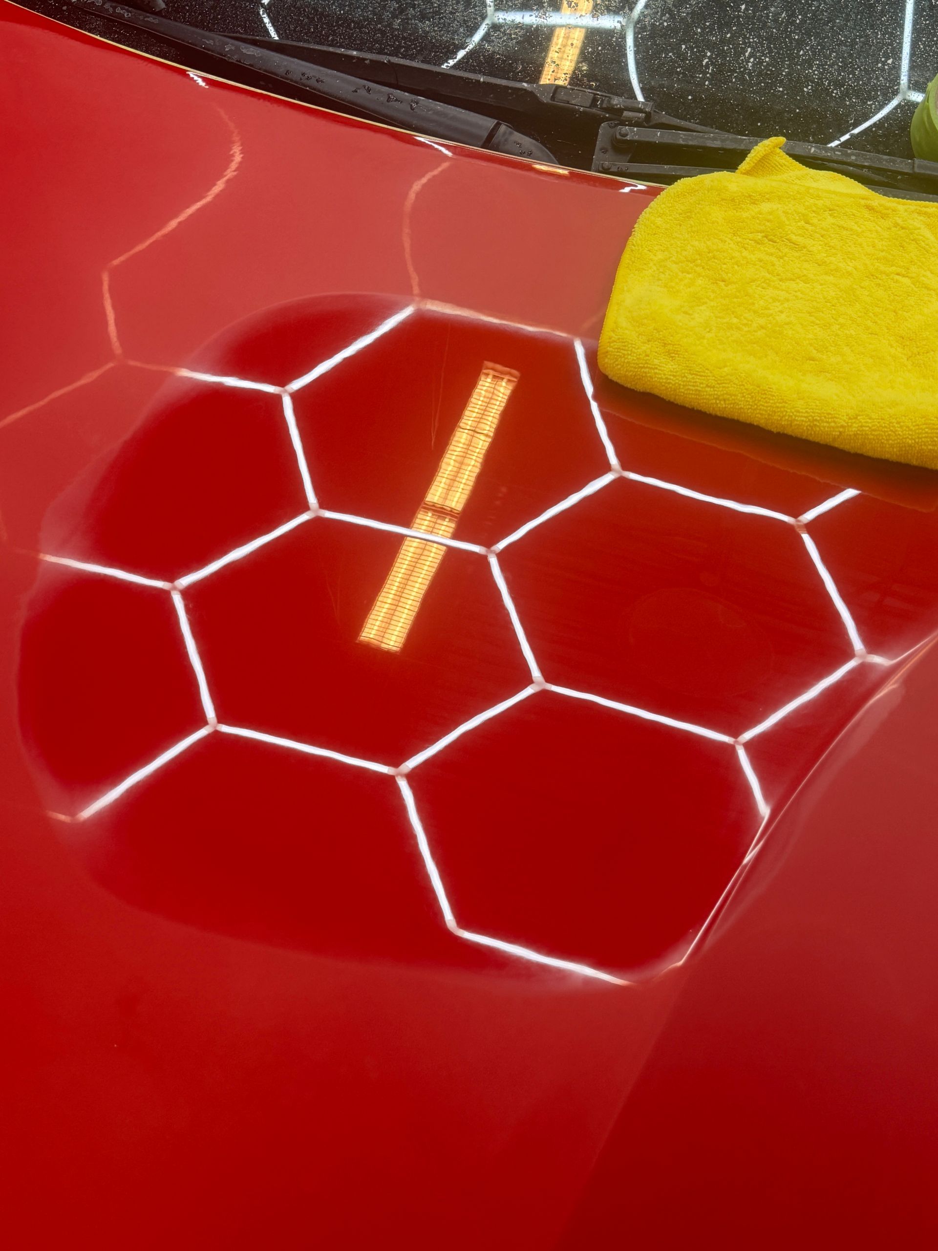 Red car hood with a honeycomb pattern and yellow microfiber cloth.