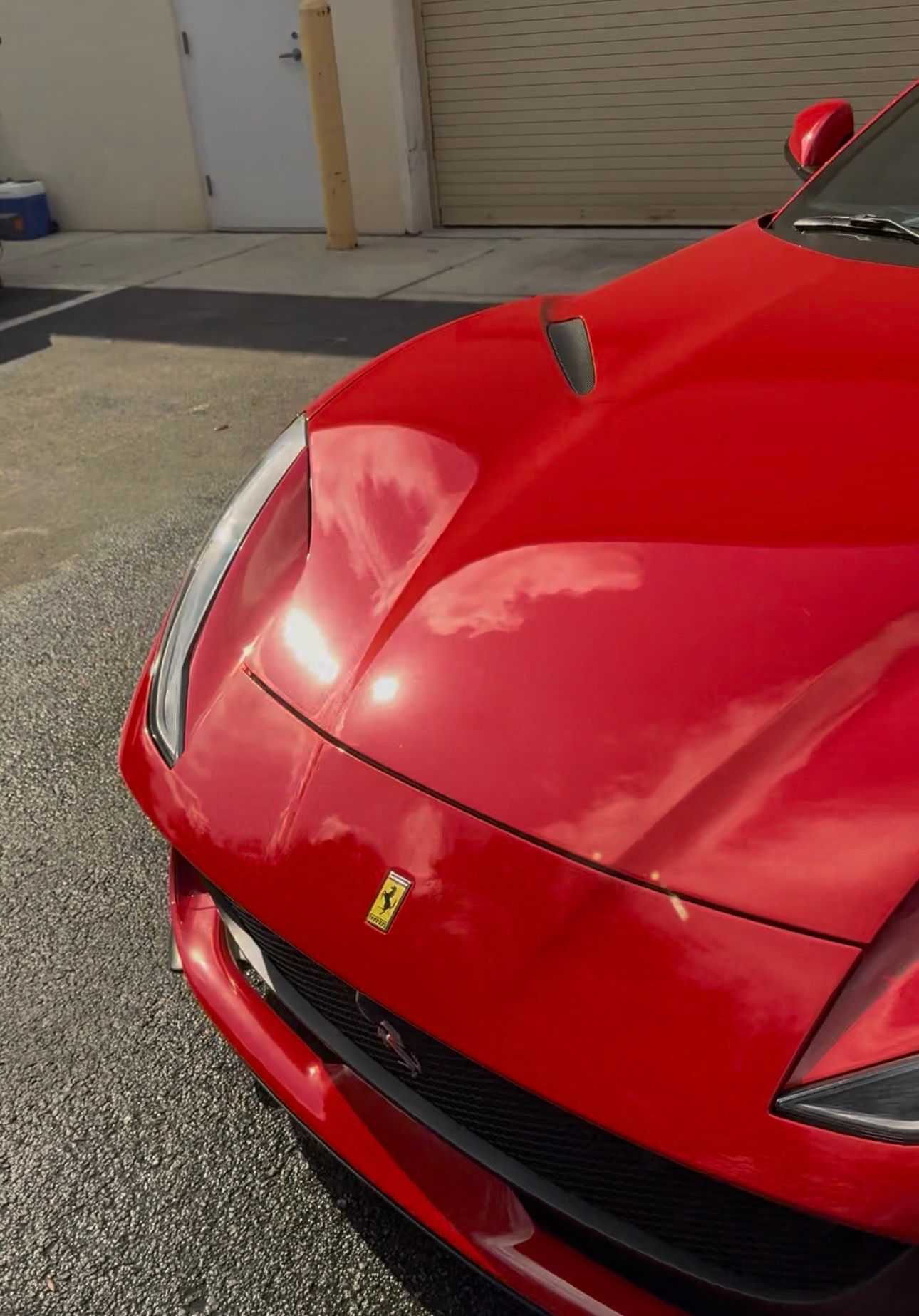 Red Ferrari sports car parked outdoors, reflecting sunlight.