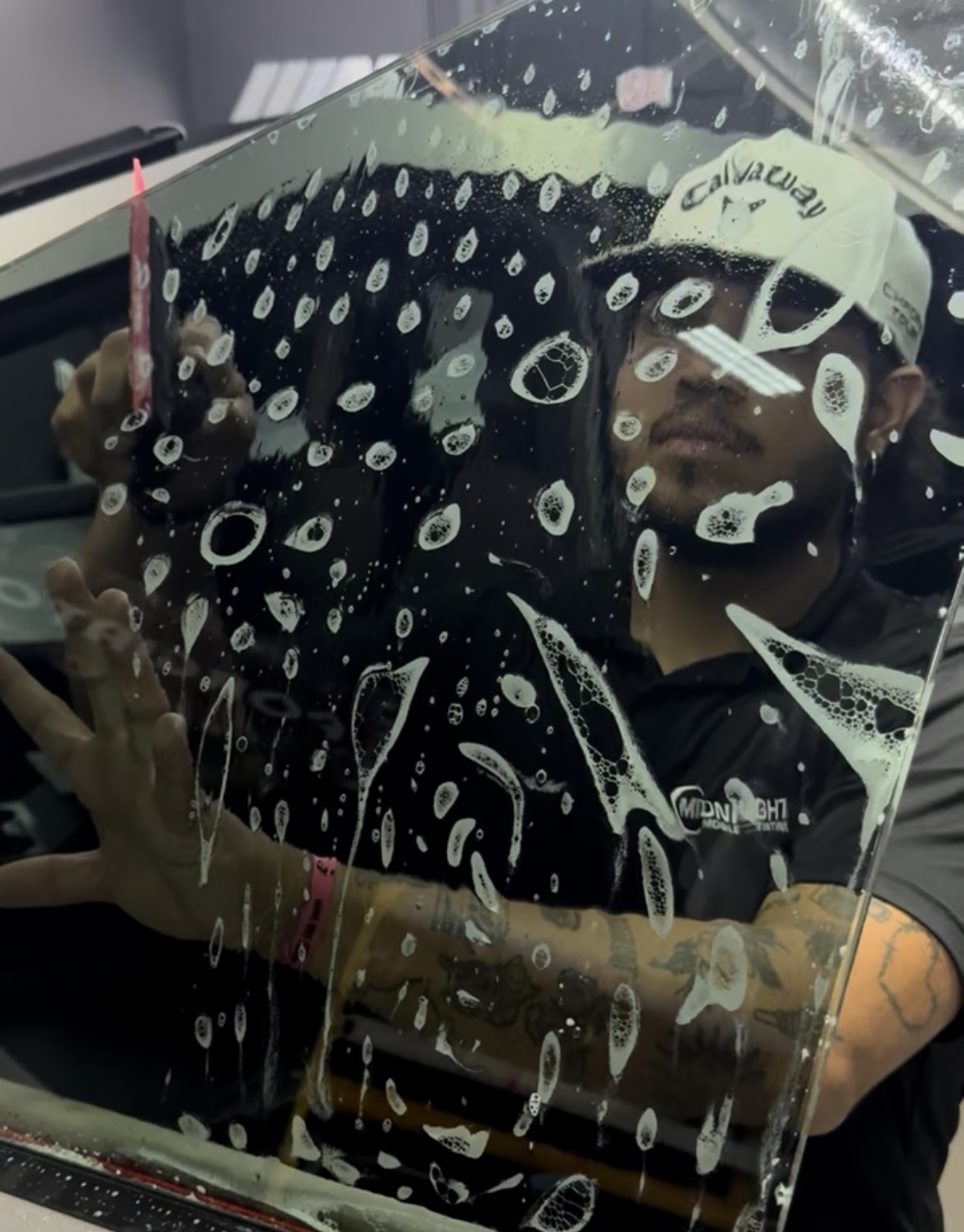 Man applying tinted film to a car window. He's holding the film with water and a squeegee.