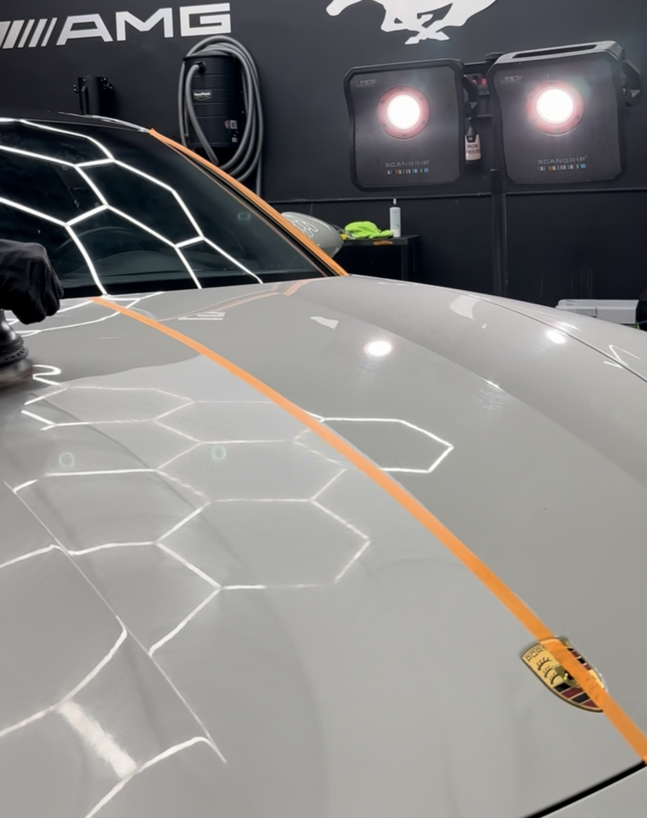 Car hood with orange tape, two bright lights, reflective surface. Detailing work in progress.