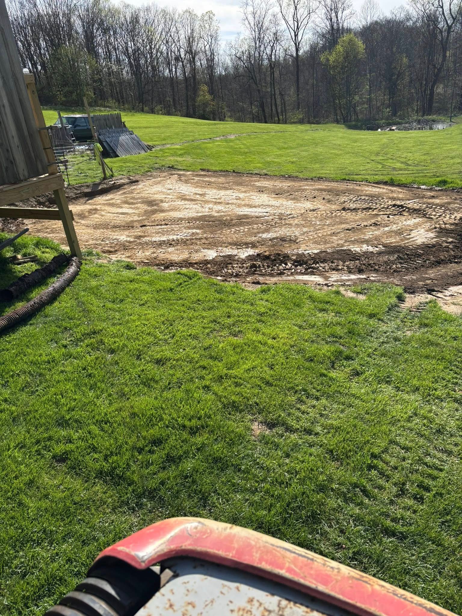 Grassy yard with a large bare dirt patch and a red lawn mower in the foreground