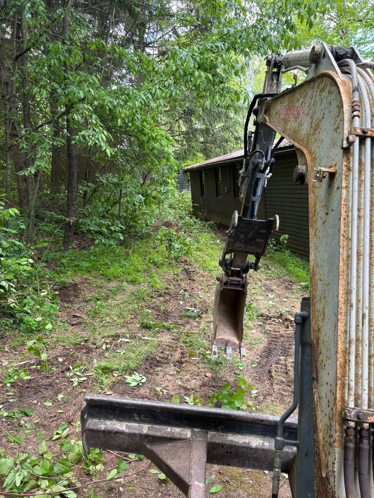Excavator arm beside a muddy forest path with dense green trees.