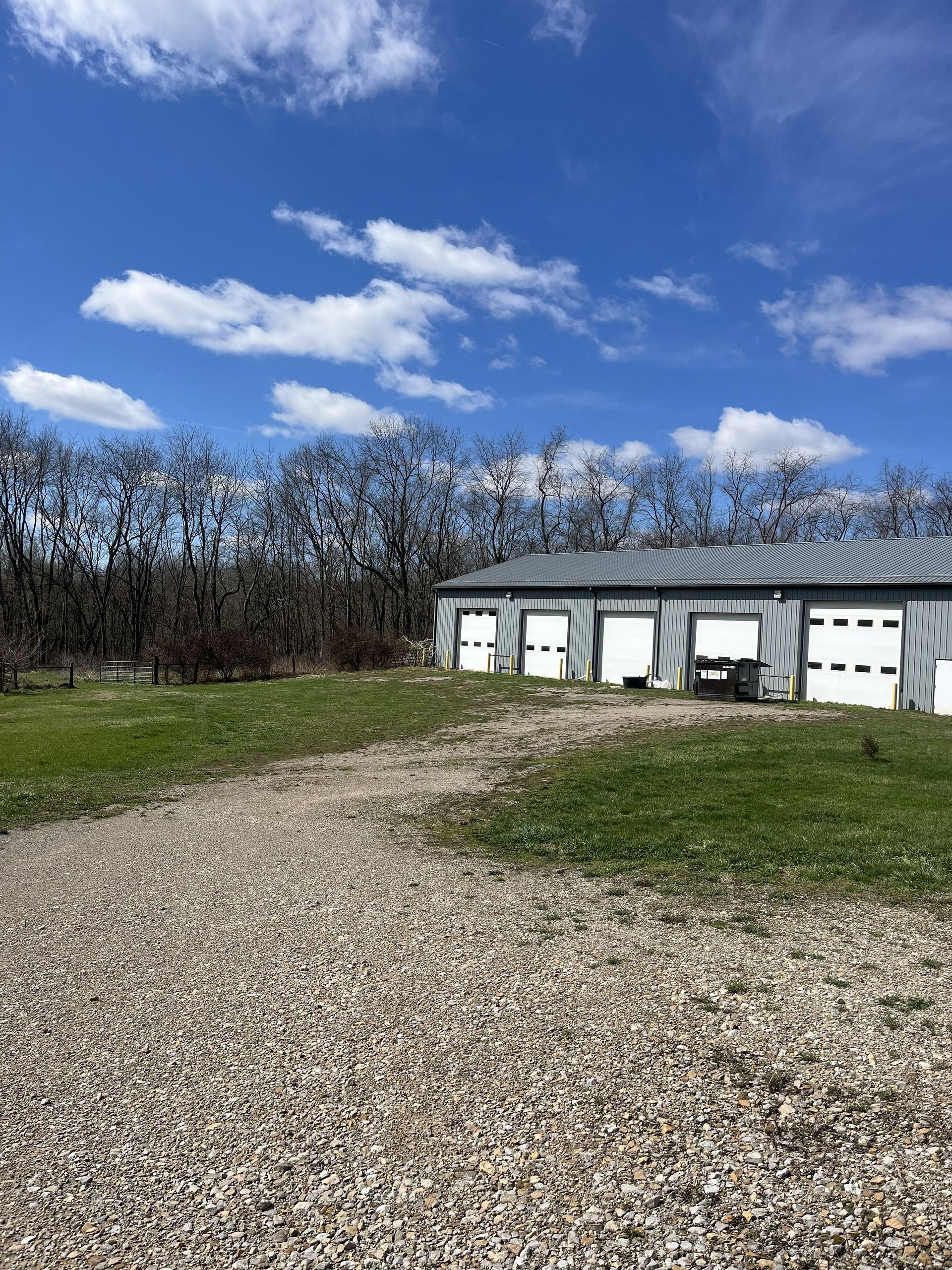 Gravel driveway leading to a row of white garage doors under a blue sky with scattered clouds.