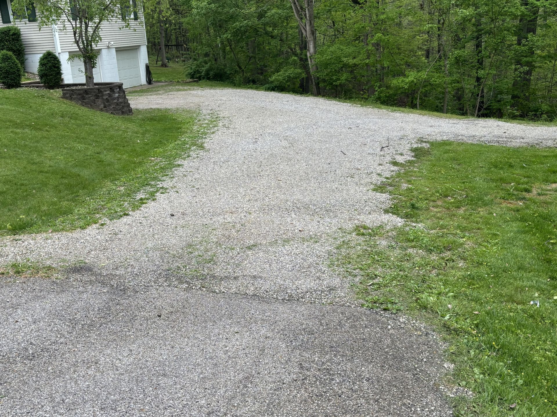 Gravel driveway curving uphill beside green grass and trees, with a white garage at left.