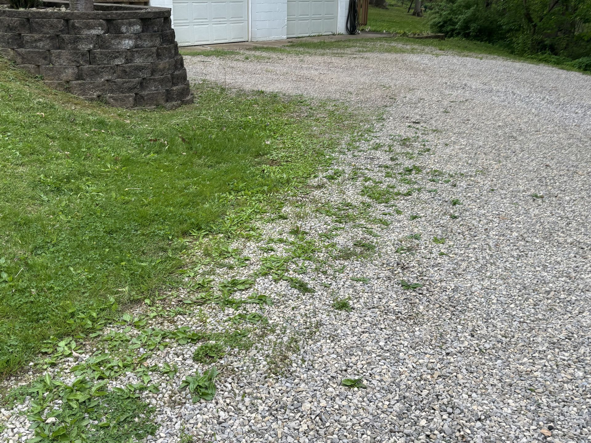 Gravel driveway curving beside a stone wall and green grass near a building