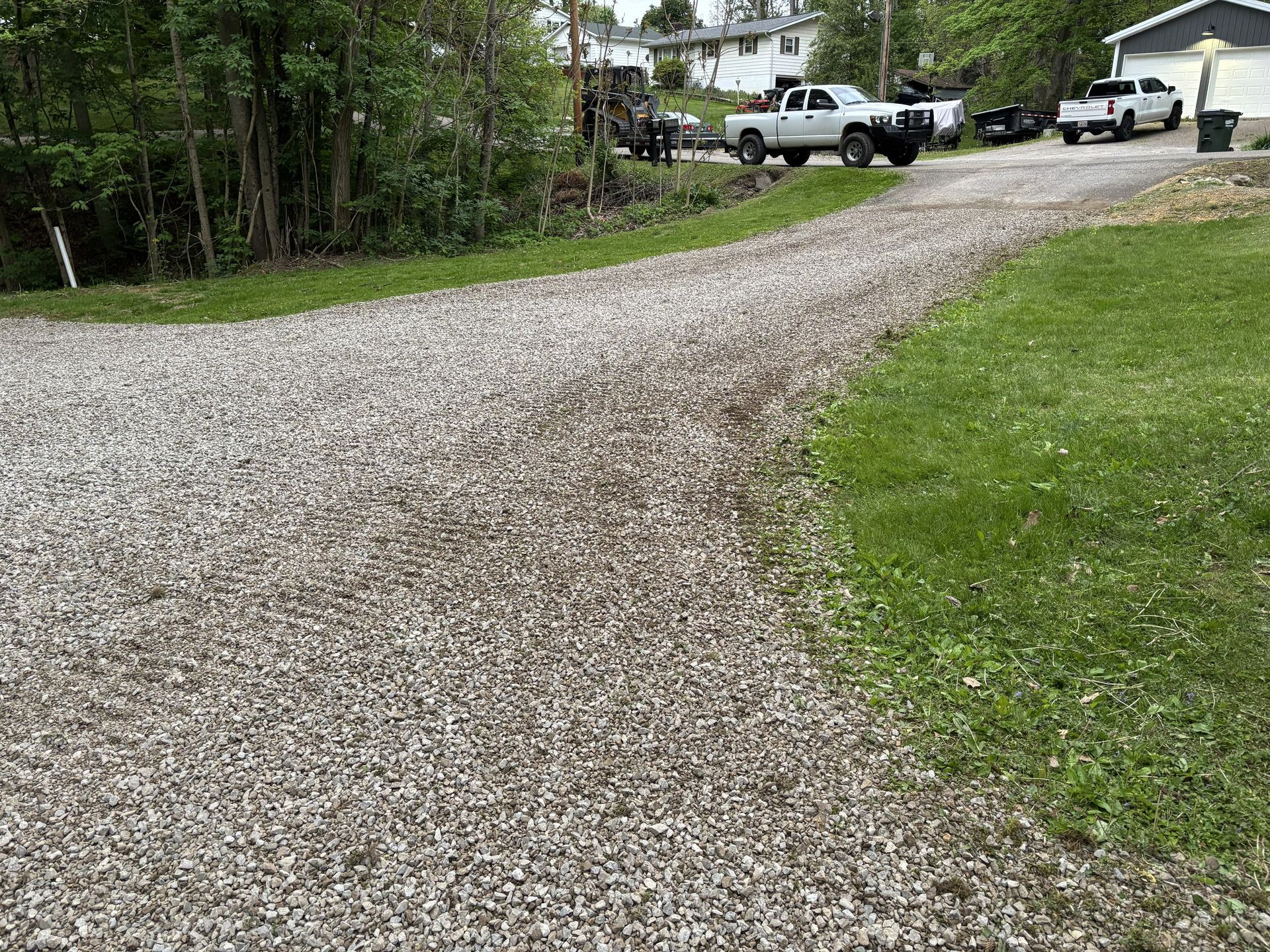 Gravel driveway curving through a wooded yard with several parked trucks near a house